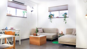 A living room with a sofa, a coffee table, a dining table with chairs, and two windows with blinds. - Chic Central TLV 1BR Near the Beach (Tel Aviv)