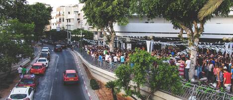 Una calle concurrida, coches estacionados y una multitud de personas reunidas cerca de un edificio.