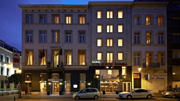 A multi-story hotel with a classic European architectural style, featuring a central entrance with a canopy, and several ground-floor shops including a library. - Leopold Hotel Brussels EU (Brussels)