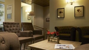 A cozy living area with a sofa, armchairs, a coffee table with a magazine, and a vase with flowers. - Leopold Hotel Brussels EU (Brussels)