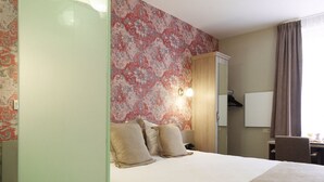 A hotel room with a bed, a wardrobe, a mirror, and a wall with a floral pattern. - Leopold Hotel Brussels EU (Brussels)