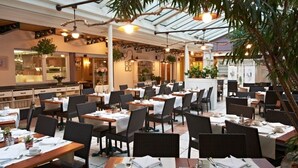 An indoor dining area with tables set for service, surrounded by chairs and plants. - Leopold Hotel Brussels EU (Brussels)