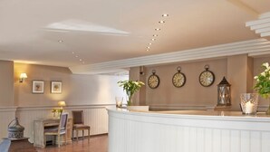 A reception area with a white reception desk, framed clocks on the wall, and a potted plant. - Leopold Hotel Brussels EU (Brussels)