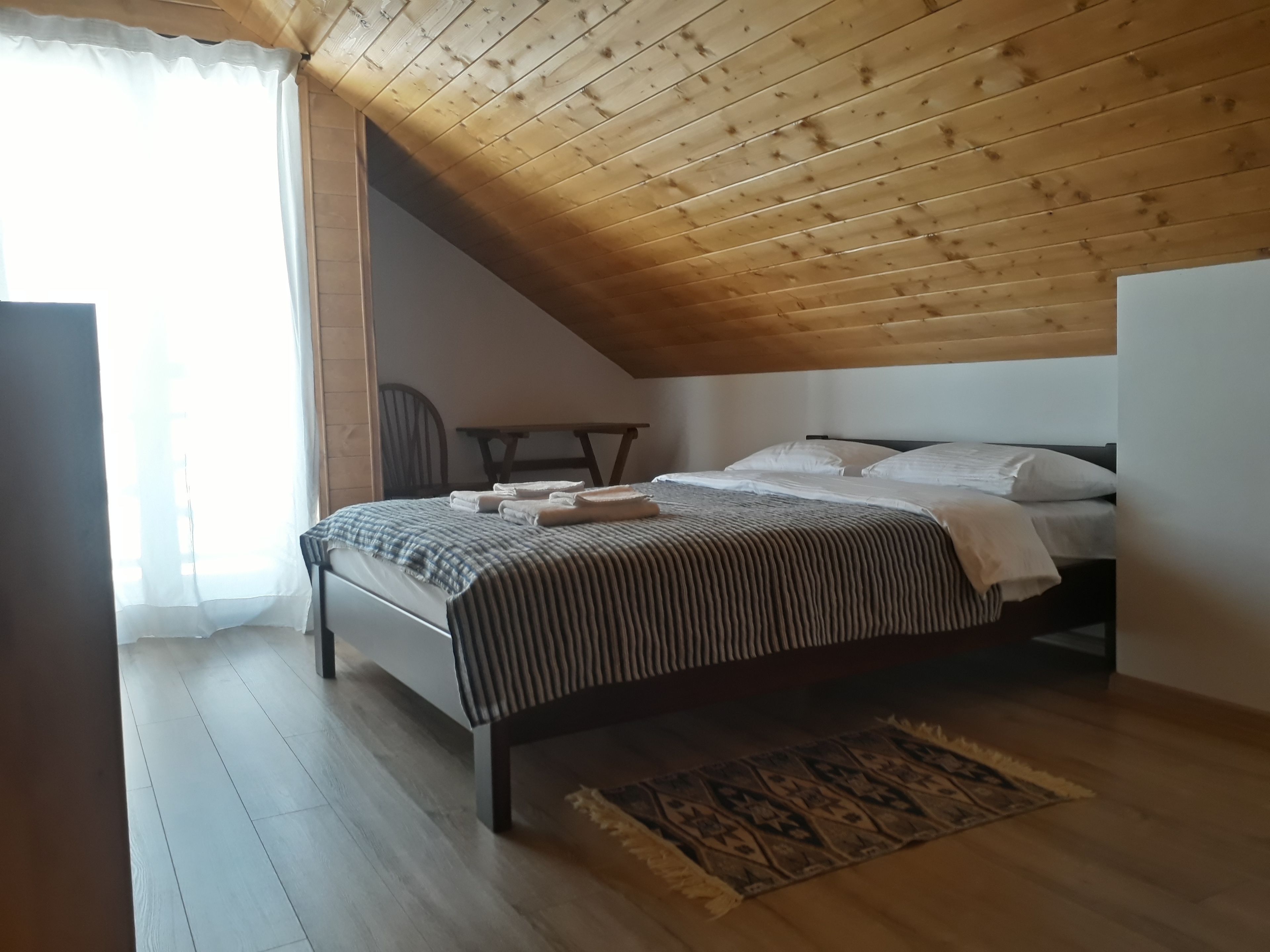 A bedroom with a sloped ceiling, a bed with a striped bedspread, a chair, and a patterned rug.