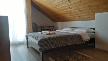 A bedroom with a sloped ceiling, a bed with a striped bedspread, a chair, and a patterned rug.