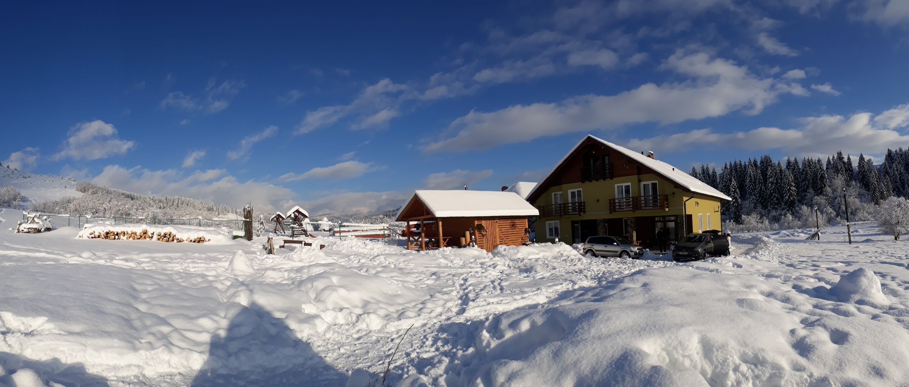 A snow-covered landscape with a large yellow house and a smaller wooden cabin.