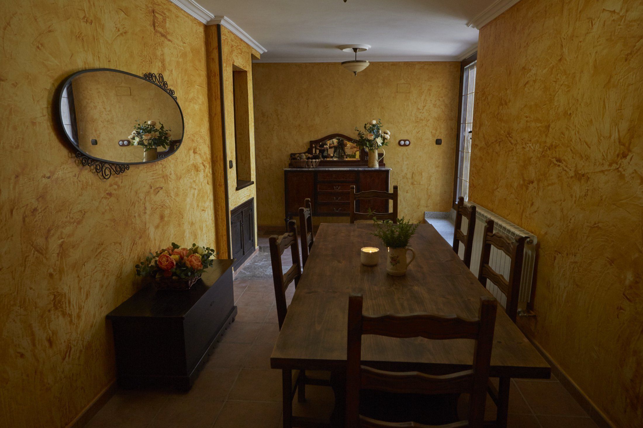 A dining room with a wooden table and chairs, a mirror on the wall, and a dresser with a mirror.