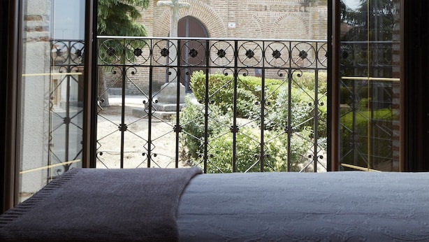 A room with a large window overlooking a traditional building with a tiled roof and a brick wall. - Posada La Casa de Las Manuelas (Horcajo de las Torres)