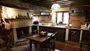 A rustic kitchen with a brick fireplace, wooden table, and chairs. - Posada La Casa de Las Manuelas (Horcajo de las Torres)