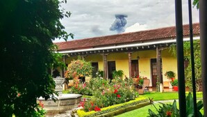 Un edificio tradicional con tejado de baldosas, porche cubierto y jardín con flores y una fuente.