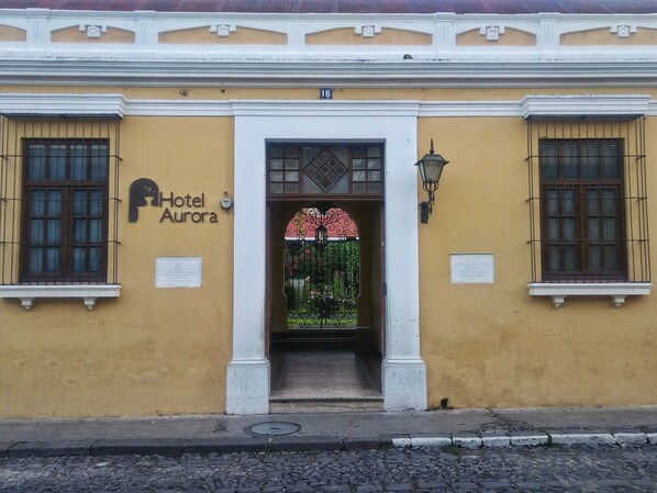 A yellow building with a sign reading "Hotel Aurora" and a decorative entrance with a glass door. - Hotel Aurora (Antigua Guatemala)