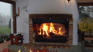 A fireplace with a fire, a table set for dining, and chairs around the table. - Pension Všeruby (Vseruby)