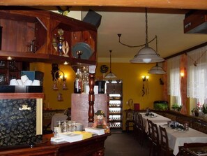 A restaurant interior with wooden furniture, pendant lighting, and a long dining table. - Pension Všeruby (Vseruby)
