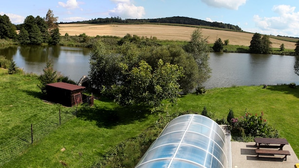 A rural landscape with a lake, green fields, a small wooden structure, and a greenhouse. - Pension Všeruby (Vseruby)