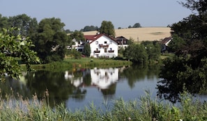 A white house with a red roof, surrounded by greenery and a calm lake. - Pension Všeruby (Vseruby)