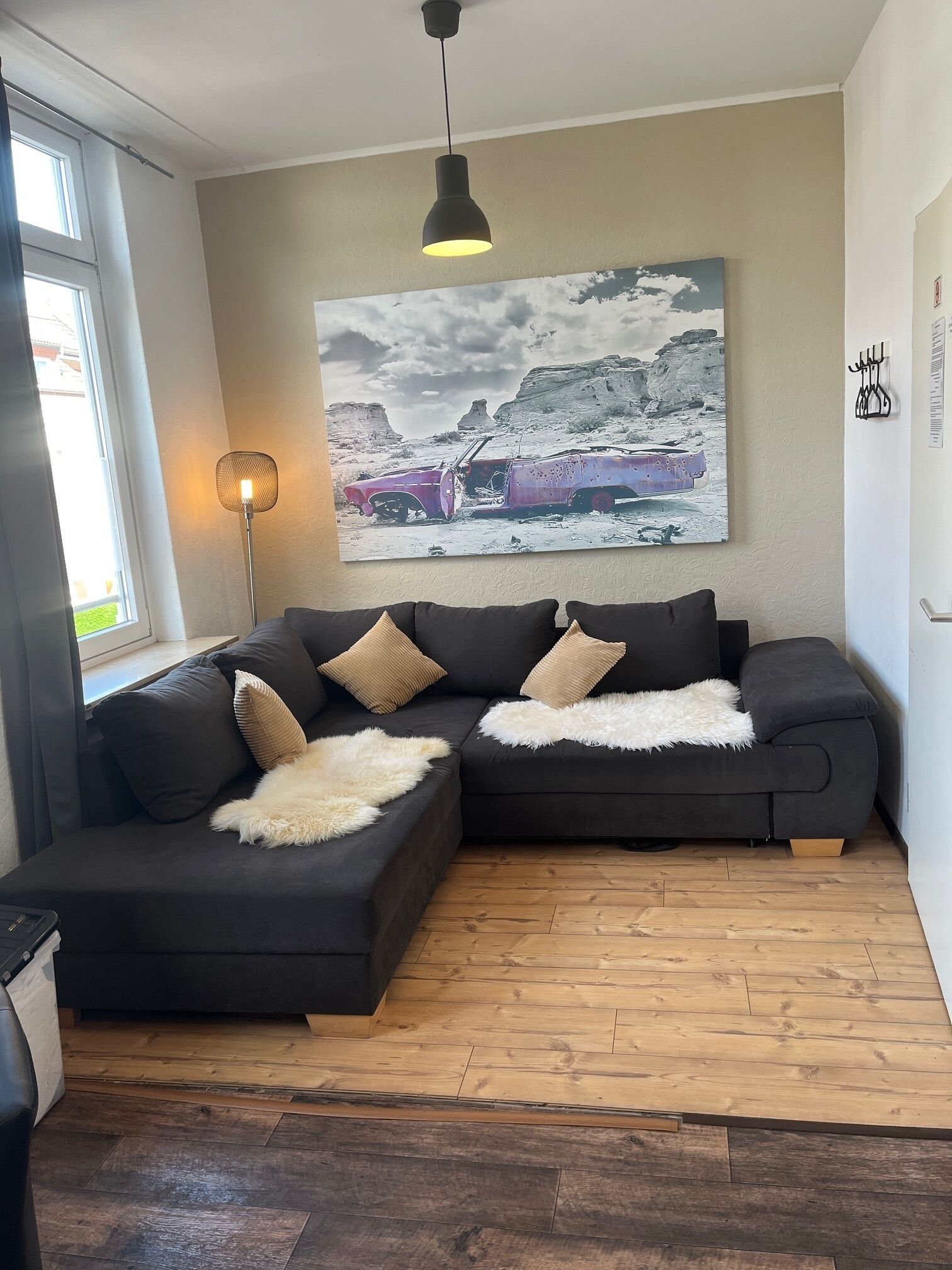 Ein modernes Wohnzimmer mit einem Ecksofa, einer Stehlampe und einem großen Landschaftsbild an der Wand.