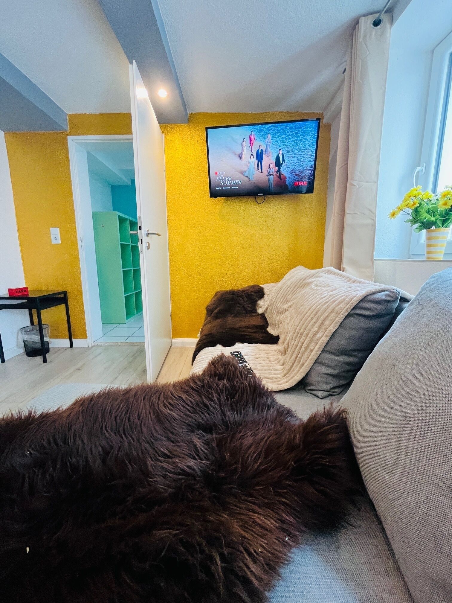A cozy room with a bed, a TV mounted on the wall, and a window with curtains.