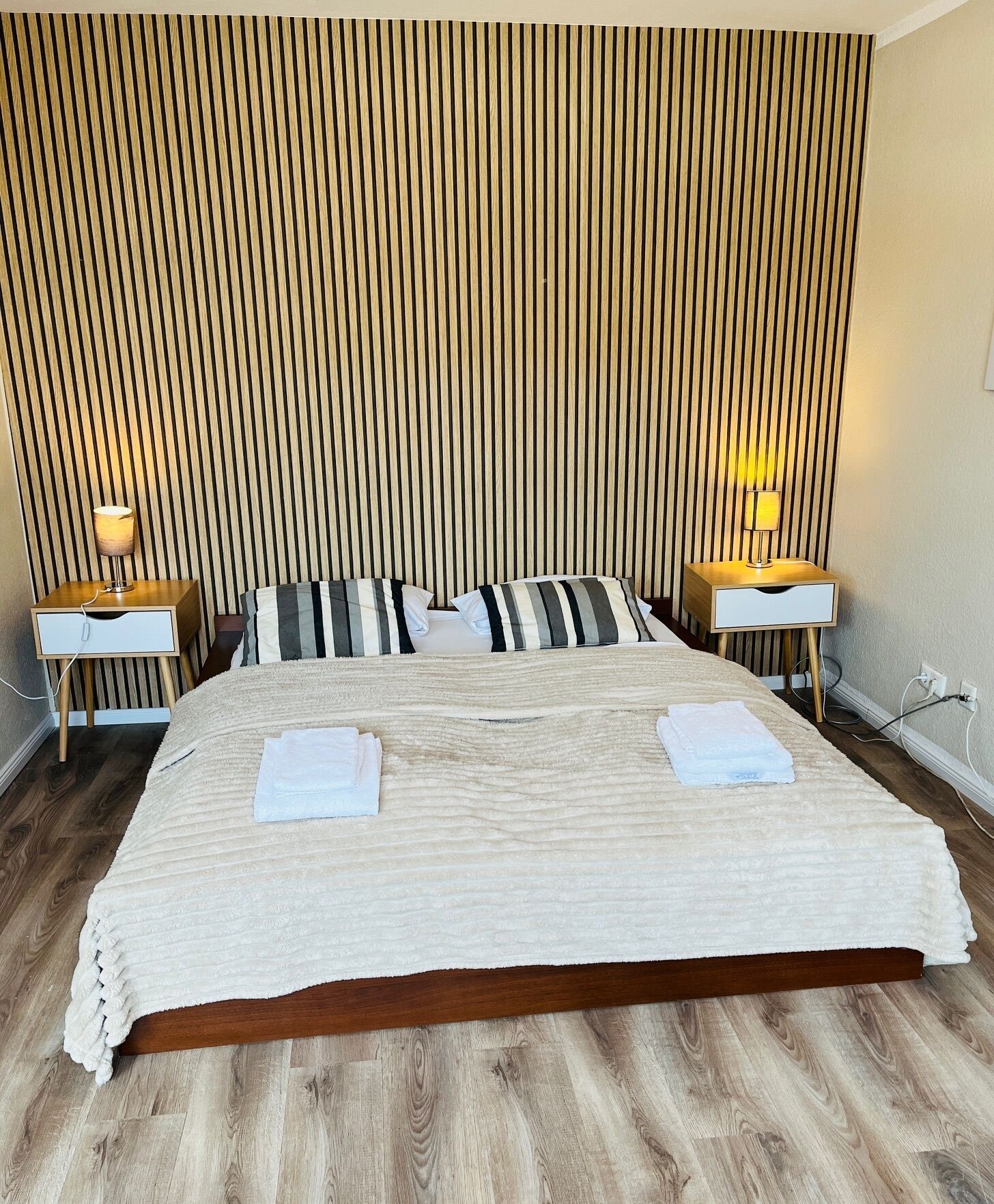 Een hotelkamer met een groot bed, twee nachtkastjes met lampen, een houten lattenbalken hoofdeinde en een houten vloer.