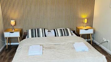 Een hotelkamer met een groot bed, twee nachtkastjes met lampen, een houten lattenbalken hoofdeinde en een houten vloer.