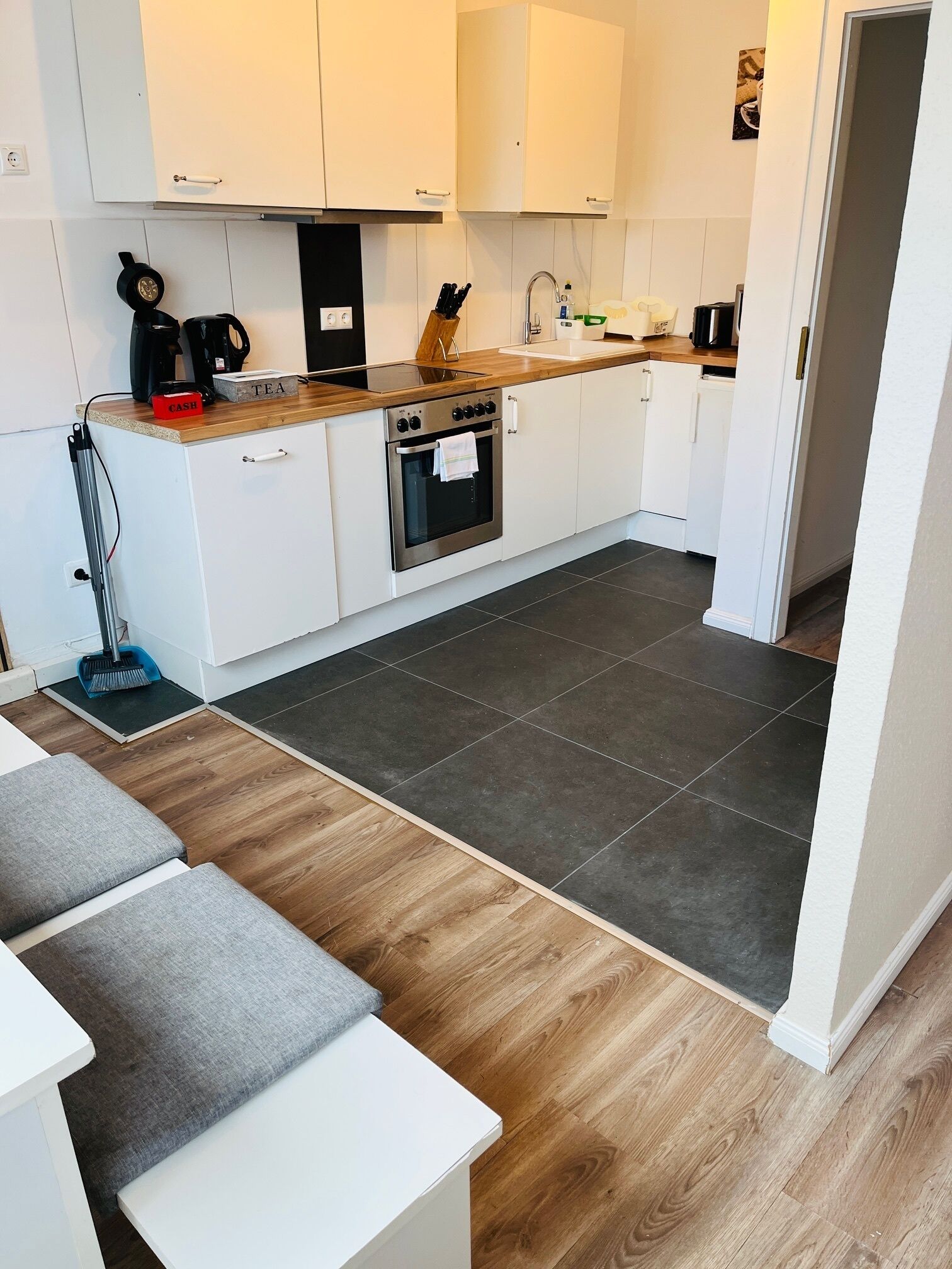 A modern kitchen with white cabinets, a wooden countertop, a built-in oven, and a coffee machine.