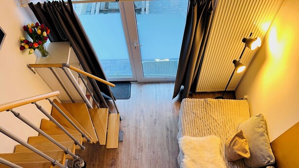 A modern interior with a wooden staircase, a sofa with cushions, and a vase of flowers. - Feldhouse (Bremen)