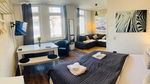 A modern hotel room with a large bed, a desk, a sofa, and a TV. - Feldhouse (Bremen)