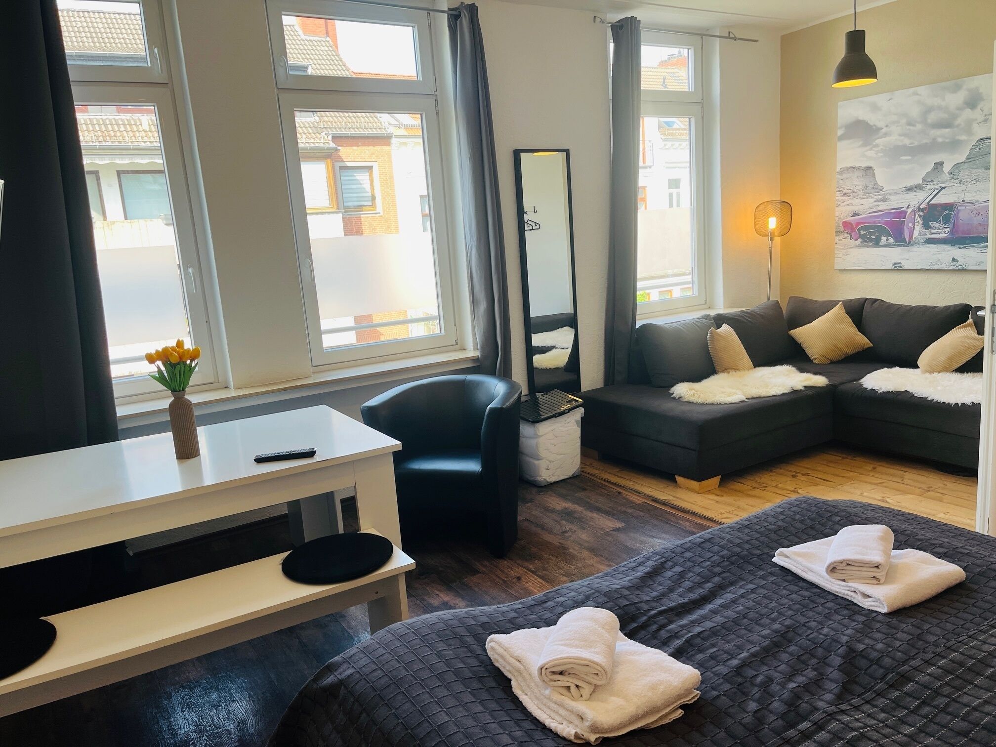 A modern hotel room with a large bed, a sofa, a desk, and a large window with curtains.