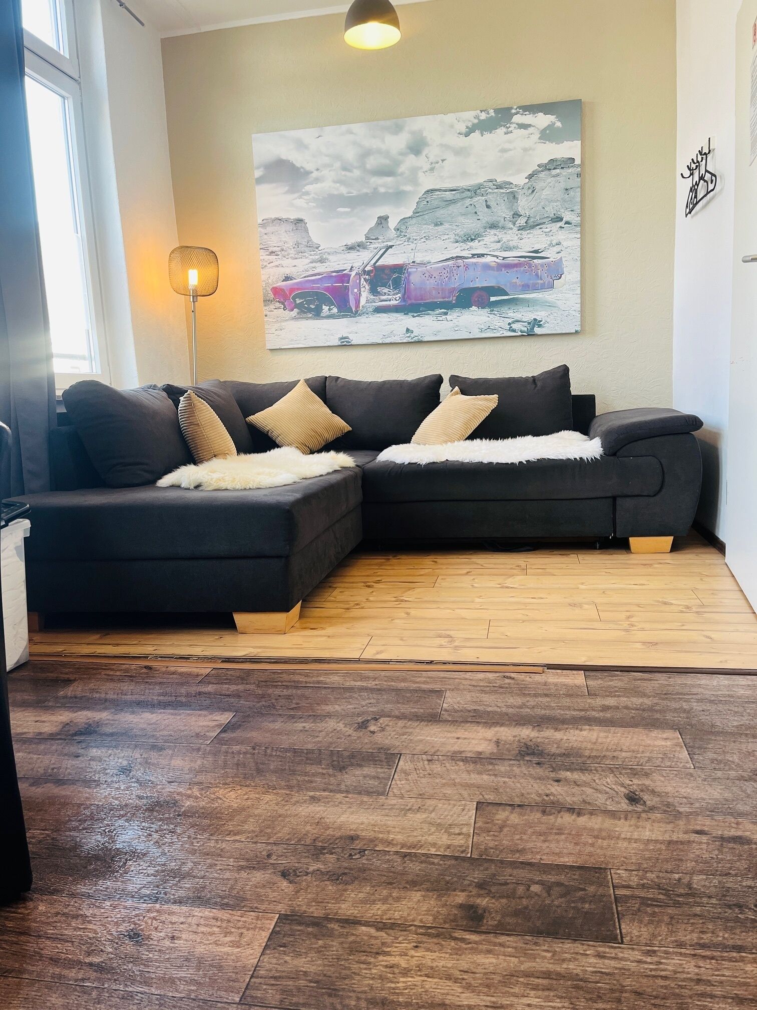 A modern living room with a sectional sofa, a floor lamp, and a large landscape painting on the wall.