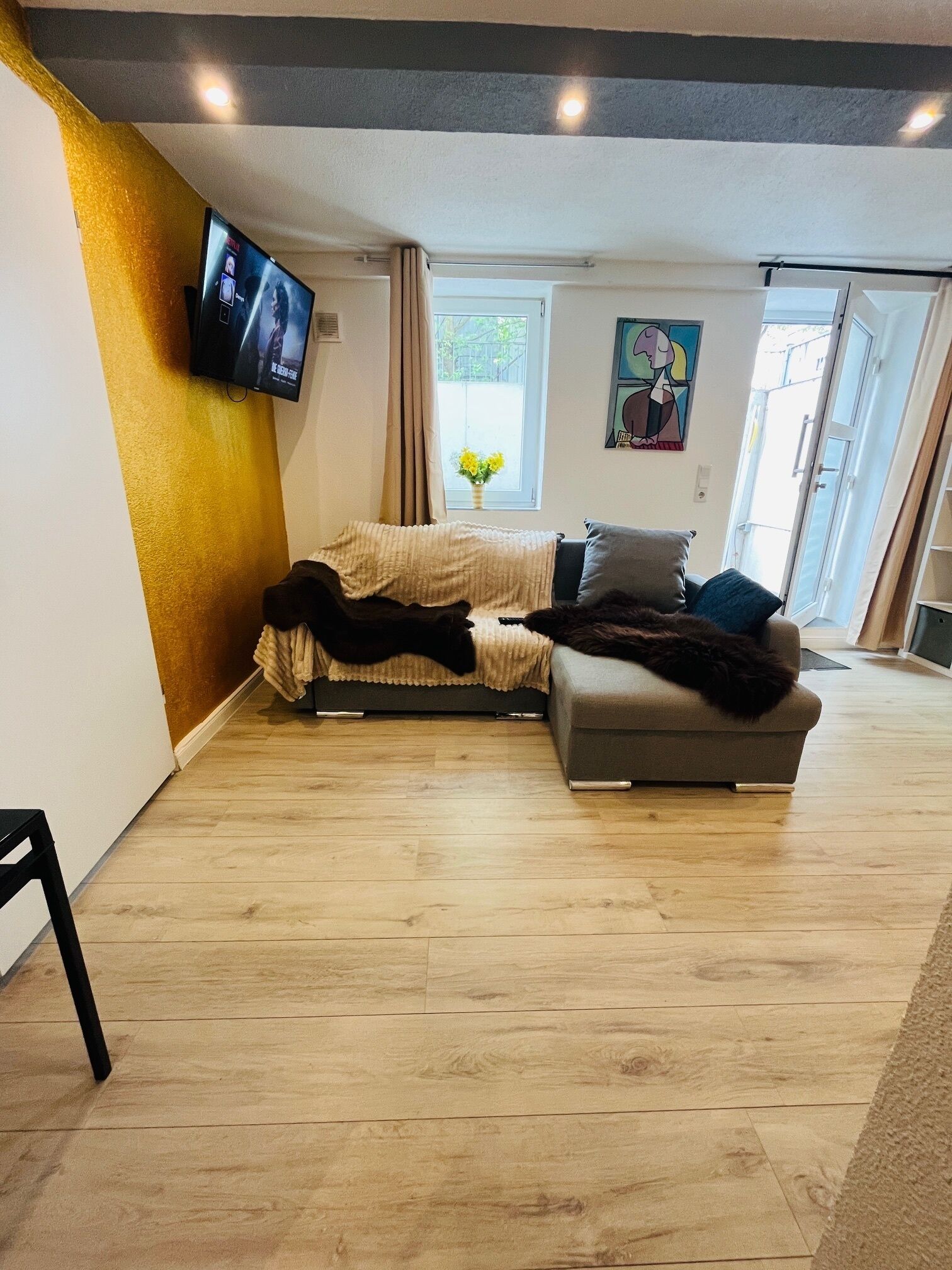 A modern living room with a sofa, a television mounted on the wall, and a window with curtains.