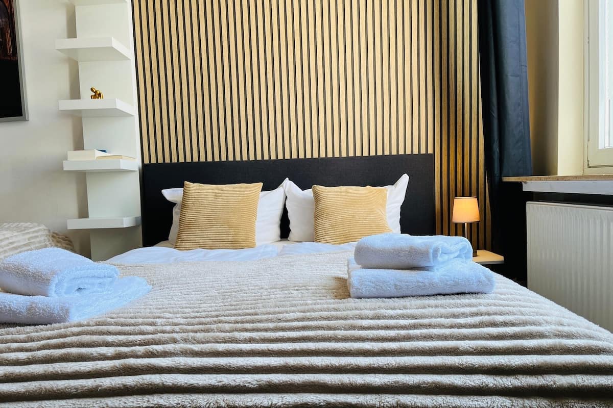 A neatly made bed with a striped blanket, two pillows, and two folded towels.