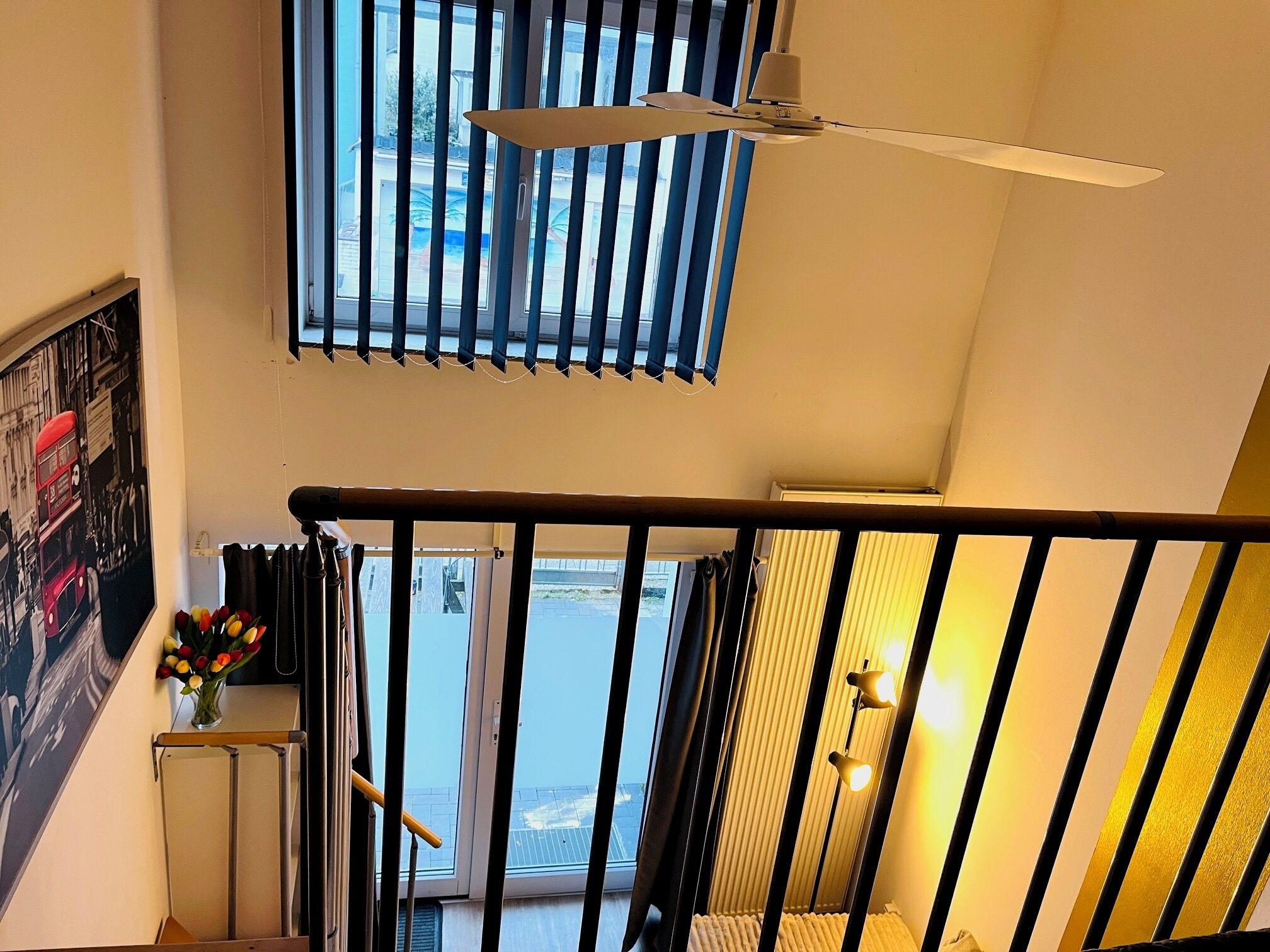 A staircase with a black railing, a ceiling fan, and a window with blinds.