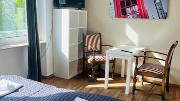 A hotel room with a bed, a desk, a chair, a television, and a painting of a red building.