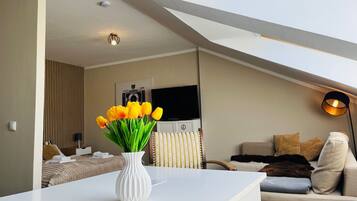A modern living room with a white table, a vase of yellow tulips, a sofa, and a television.