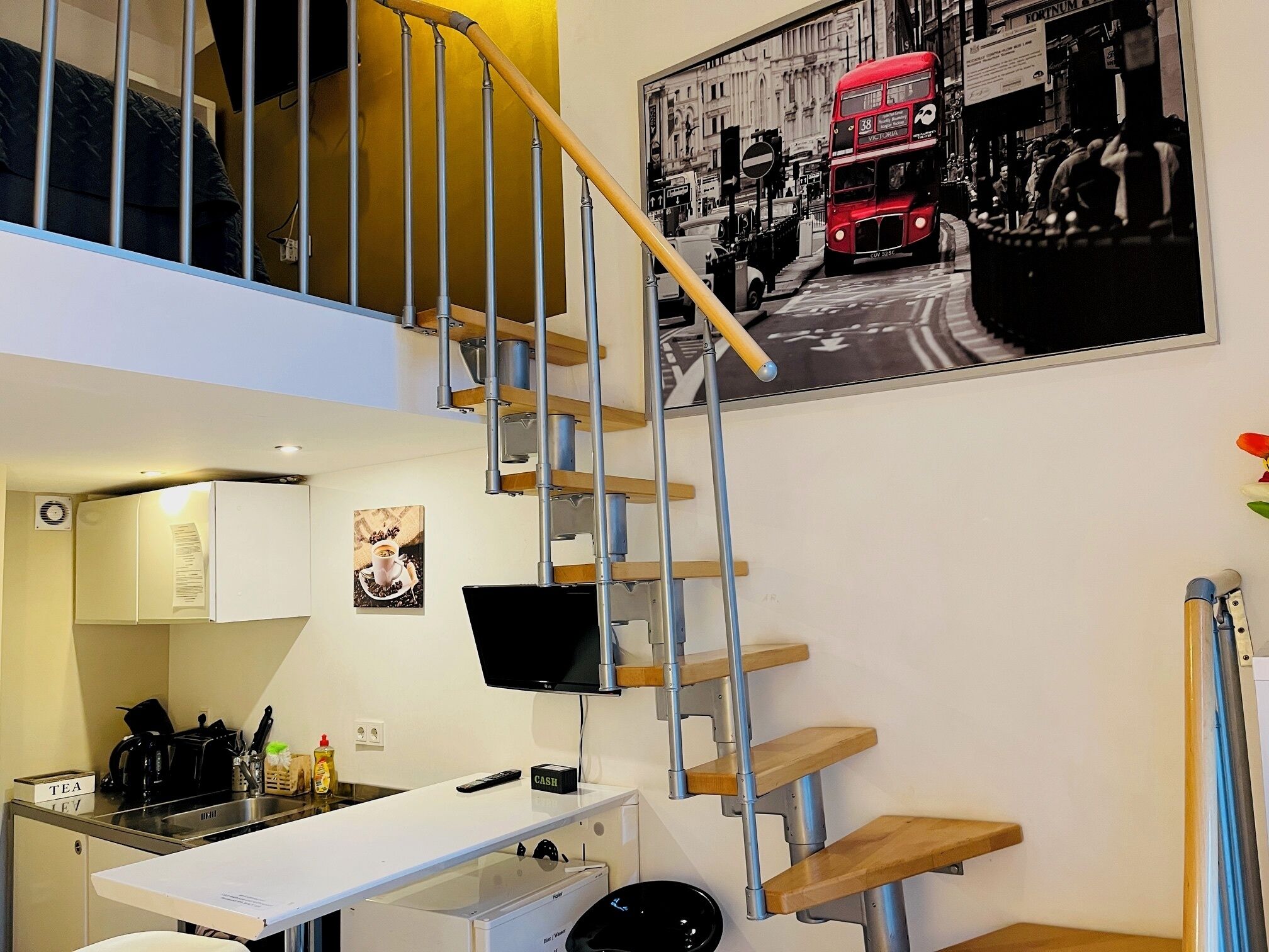 A modern kitchen with a built-in stove, a coffee machine, and a small dining table. A staircase with a wooden handrail leads to an upper level.
