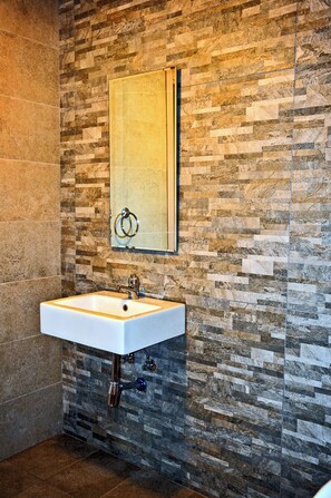 Un baño con pared de diseño de piedra, un espejo rectangular y un lavabo blanco con un solo grifo.