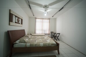 A bedroom with a bed, a desk, a chair, a ceiling fan, and a window with curtains.
