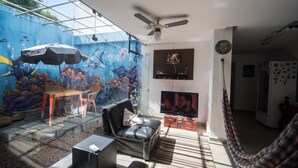 A living room with a mural, a television, a ceiling fan, and a hammock. - Hostel do Bosque (Rio de Janeiro)