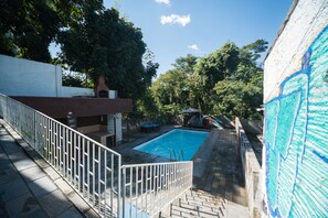 A swimming pool with a white fence, surrounded by trees and a building with a brick chimney.
