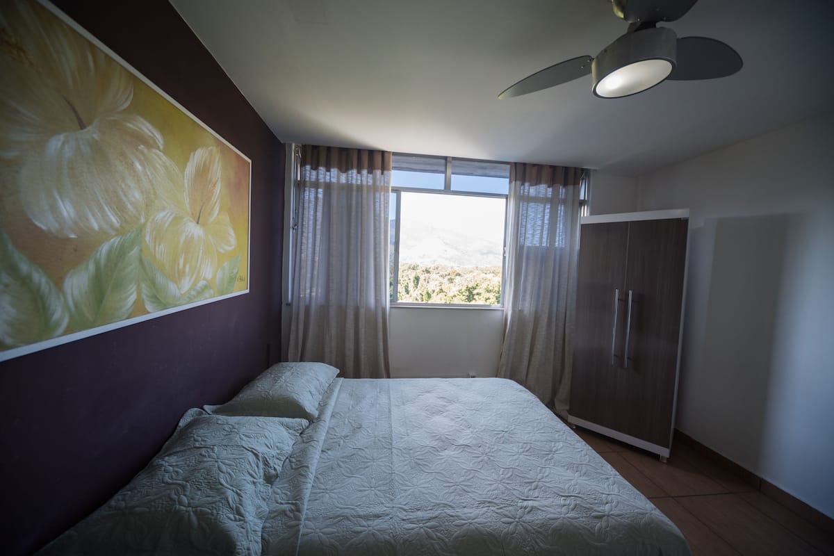 Ein Schlafzimmer mit Bett, Deckenventilator, Kleiderschrank und einem fenster mit Vorhängen.