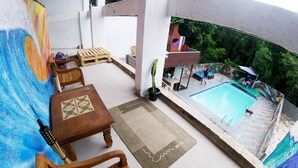 A balcony with a pool, wooden furniture, and a view of the pool area. - Hostel do Bosque (Rio de Janeiro)