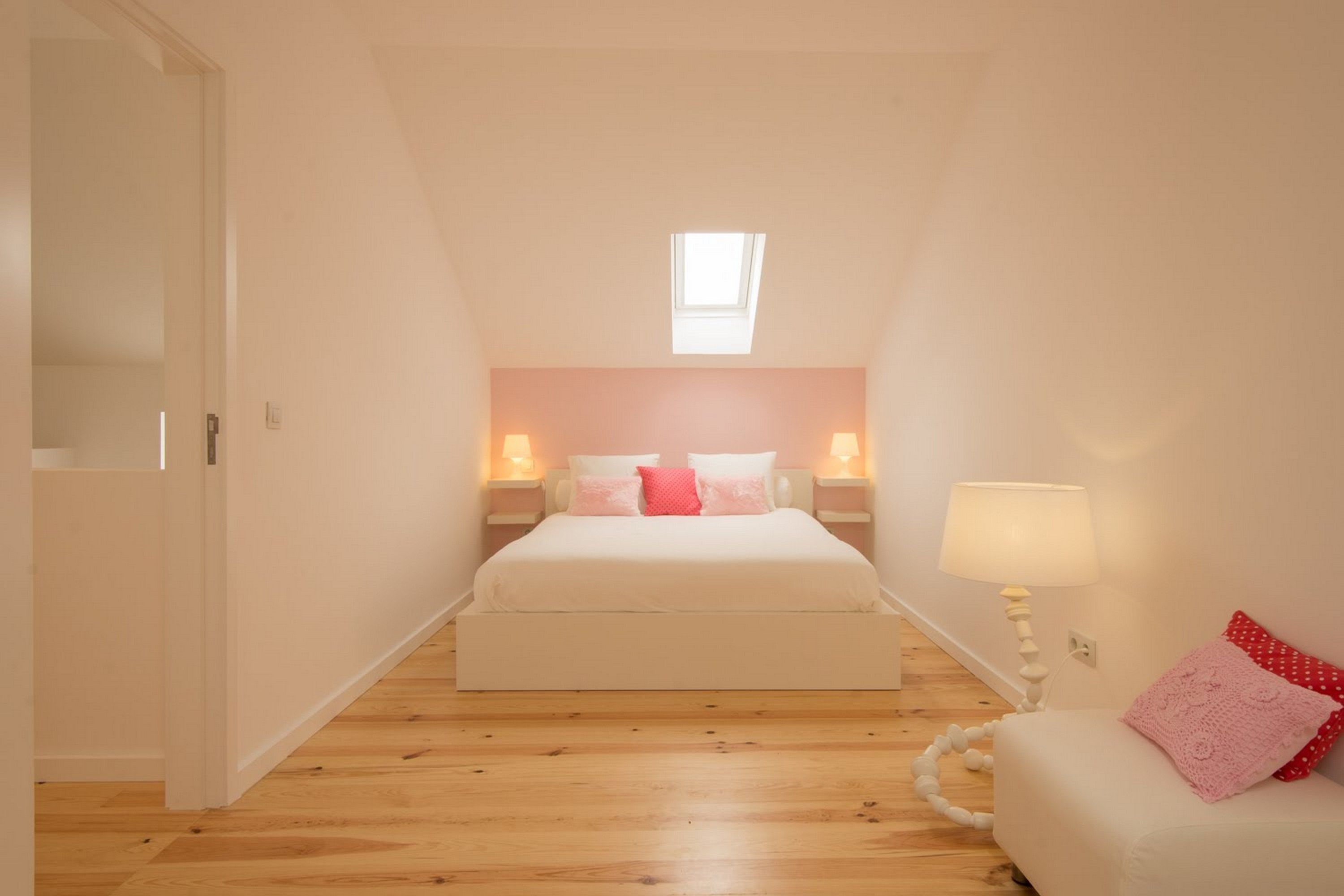 A bedroom with a bed, bedside lamps, a window, and a door.