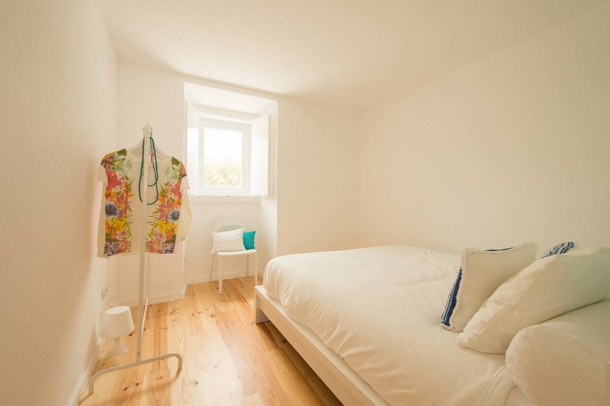 A bedroom with a bed, a window, a chair, and a small table.