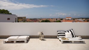 A rooftop terrace with a white wall, a lounge area with a white lounger, a small table with a tray, and a decorative lantern. - Casasupertubos (Peniche)