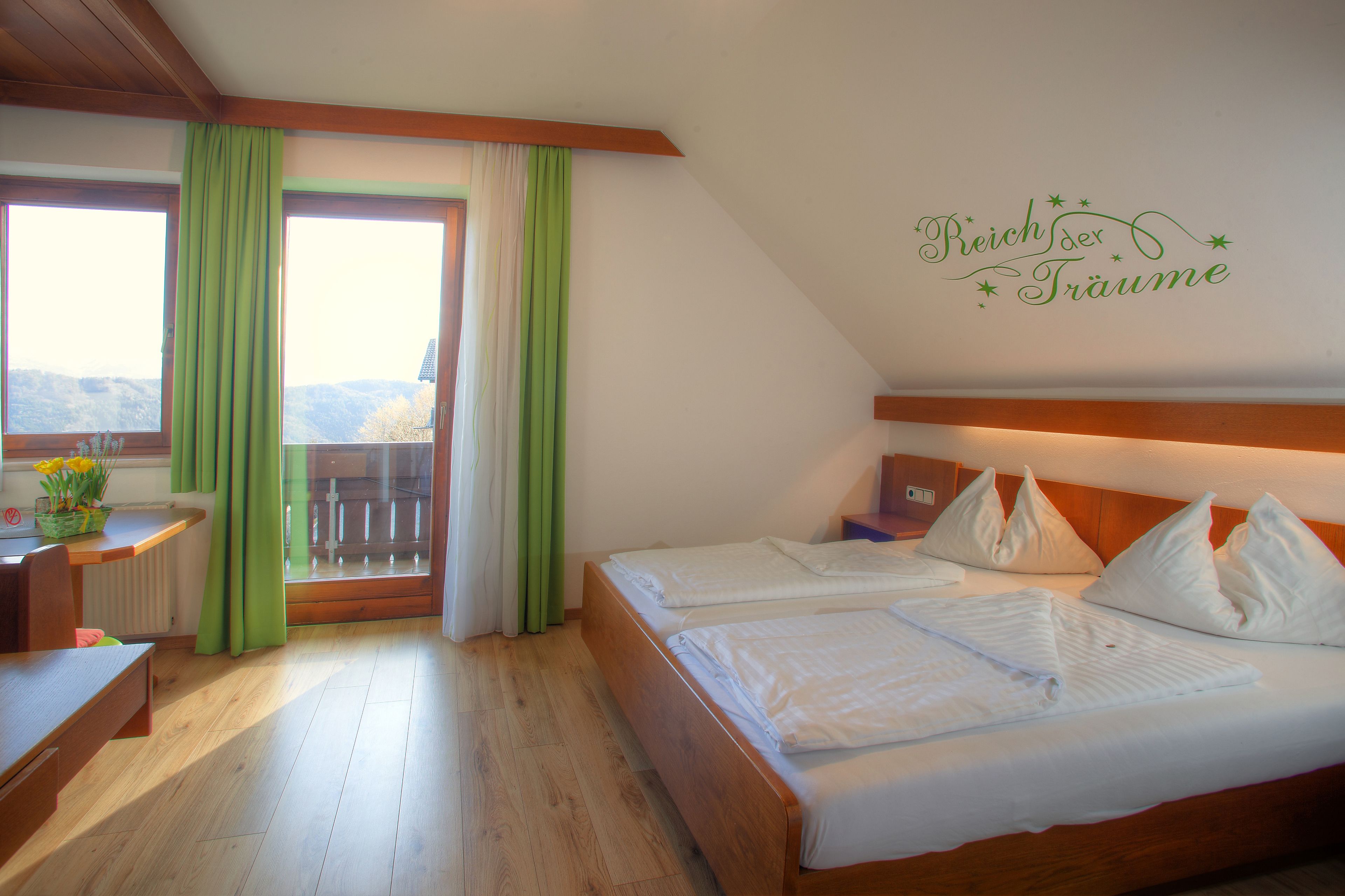 Habitación de hotel con dos camas, un escritorio de madera, una silla, una ventana con cortinas y un balcón.