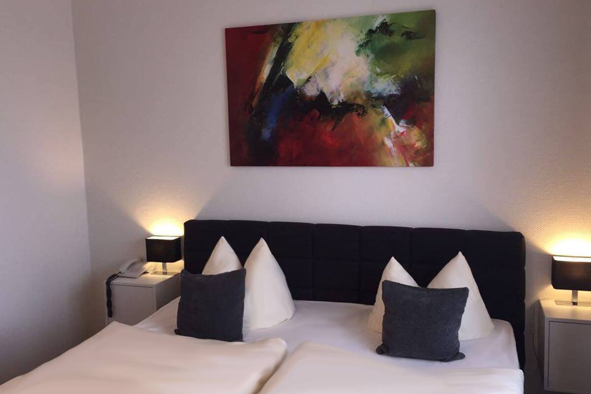 A hotel room with a large bed, two bedside tables, and a colorful abstract painting on the wall.