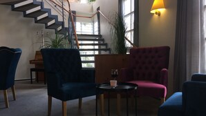 Un moderno vestíbulo de hotel con una escalera, asientos cómodos y una mesa con una copa de vino.