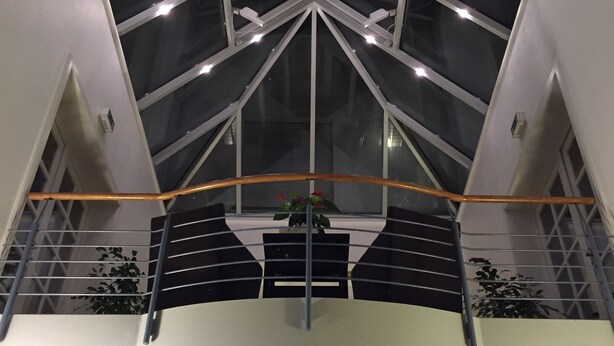 Un interior moderno con techo alto, paneles de vidrio geométricos y una escalera central.