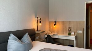 Habitación de hotel con una cama, un escritorio y una silla. Hay una lámpara en el escritorio y un teléfono en la pared.