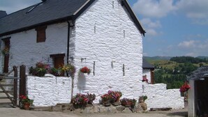 Un edificio de piedra blanca con techo inclinado, puerta de madera y flores en macetas.