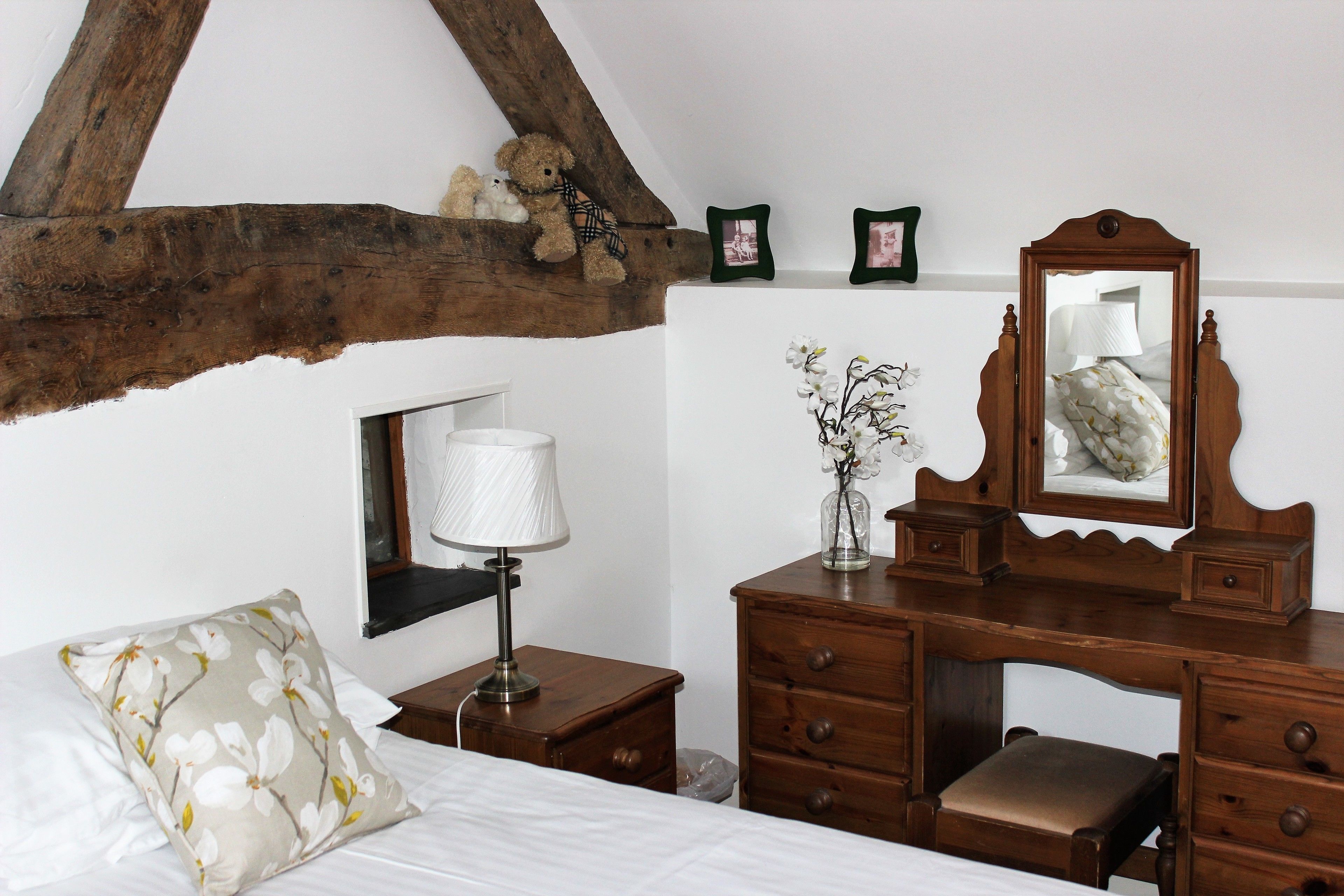 A bedroom with a wooden headboard, a bed with white bedding, a nightstand with a lamp, a dresser with drawers, and a mirror.